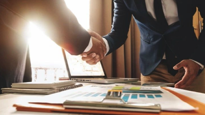 Two people shaking hands over a laptop.